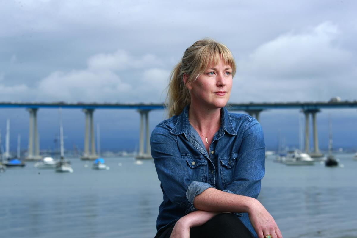 Maggie Shipstead sits in front of a bridge over water with boats floating.