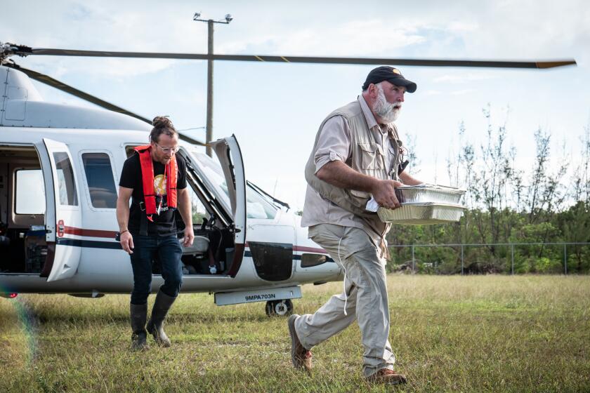 Two men, one carrying trays of food, exit a helicopter in the documentary "We Feed People."