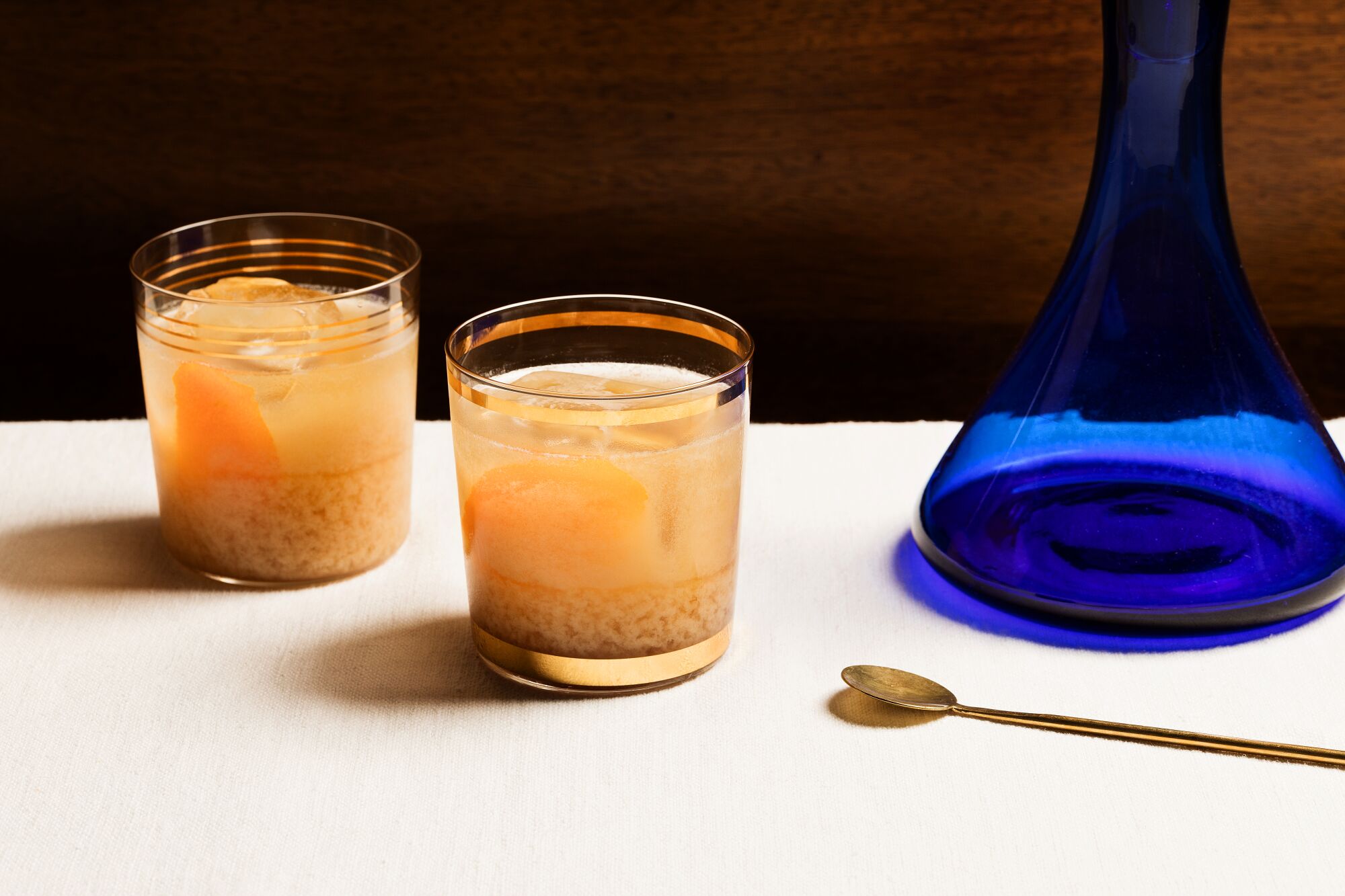 Two cocktail glasses with a light brown drink next to a blue glass vase.