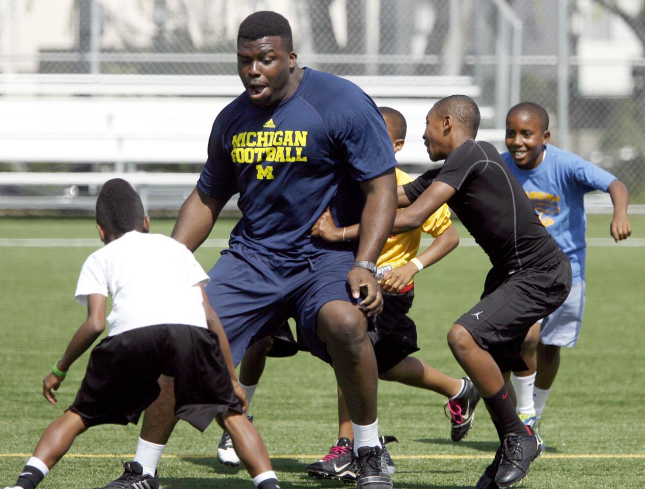University of Michigan DL Will Campbell tries to get away from a crowd of young tacklers during workout with about 80 local youth as part of Pasadena's Youth Camp Mentoring Program at Robinson Park in Pasadena on Thursday, May 24, 2012.