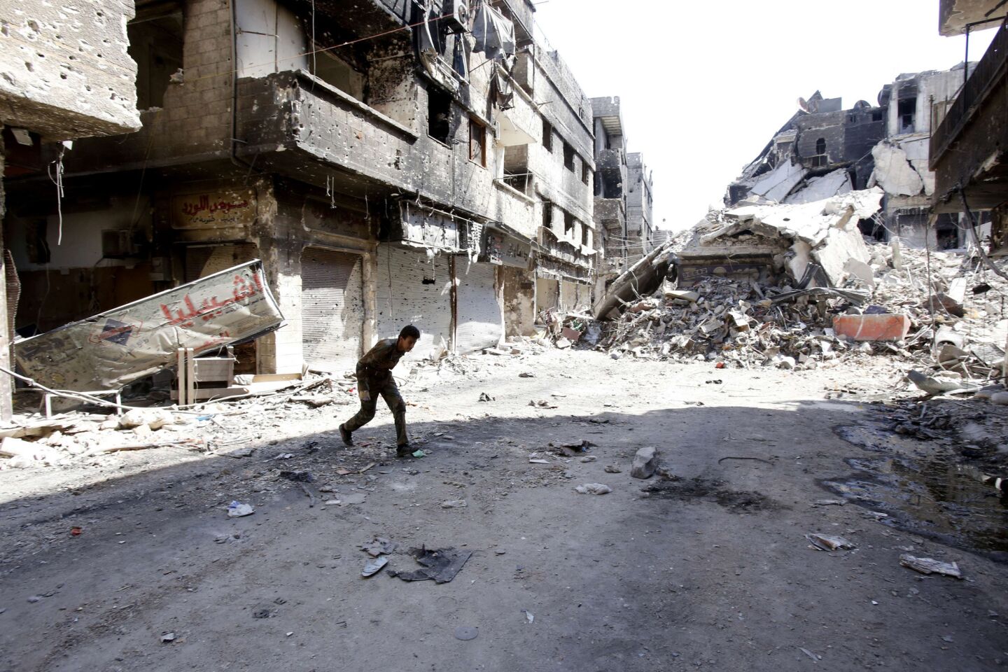 A fighter allied with Syrian President Bashar Assad runs across the street after fighting with rebels in the Yarmouk refugee camp in the capital, Damascus.
