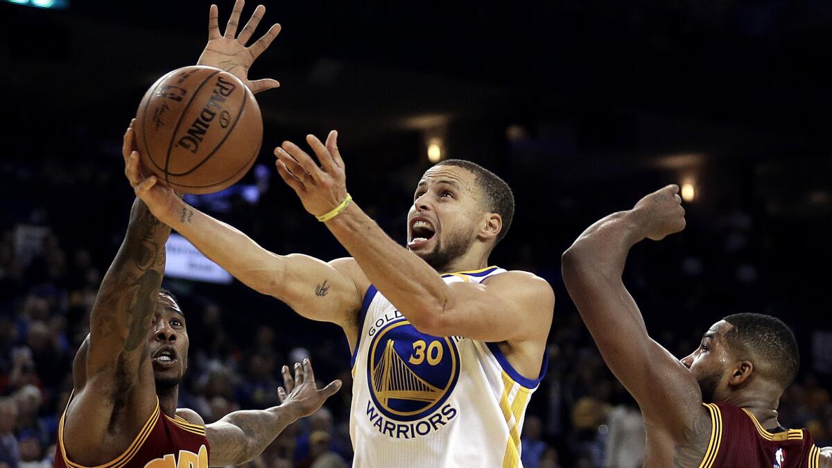 Warriors point guard Stephen Curry splits the defense of Cavaliers forwards Iman Shumpert, left, and Tristan Thompson for a layup during the second half Monday.