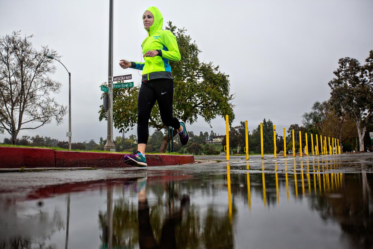 A jogger runs in the rain at the Rose Bowl loop trail March 19, 2020.