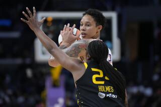 Mercury center Brittney Griner holds up the ball while Sparks player Joyner Holmes raises her arm to block Griner's view