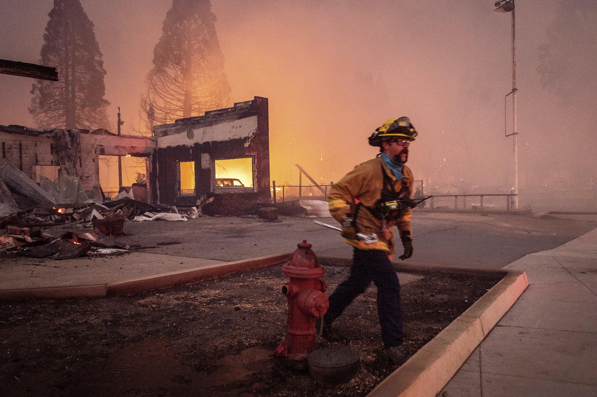 A firefighter walks past buildings destroyed by the Dixie fire in Greenville, Calif.