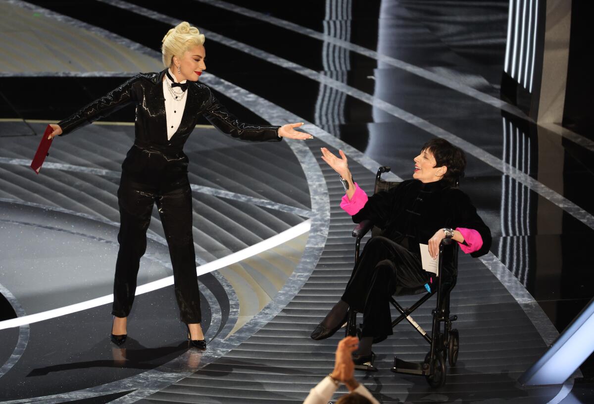 A woman in a tux reaches out on stage to a woman in a wheelchair