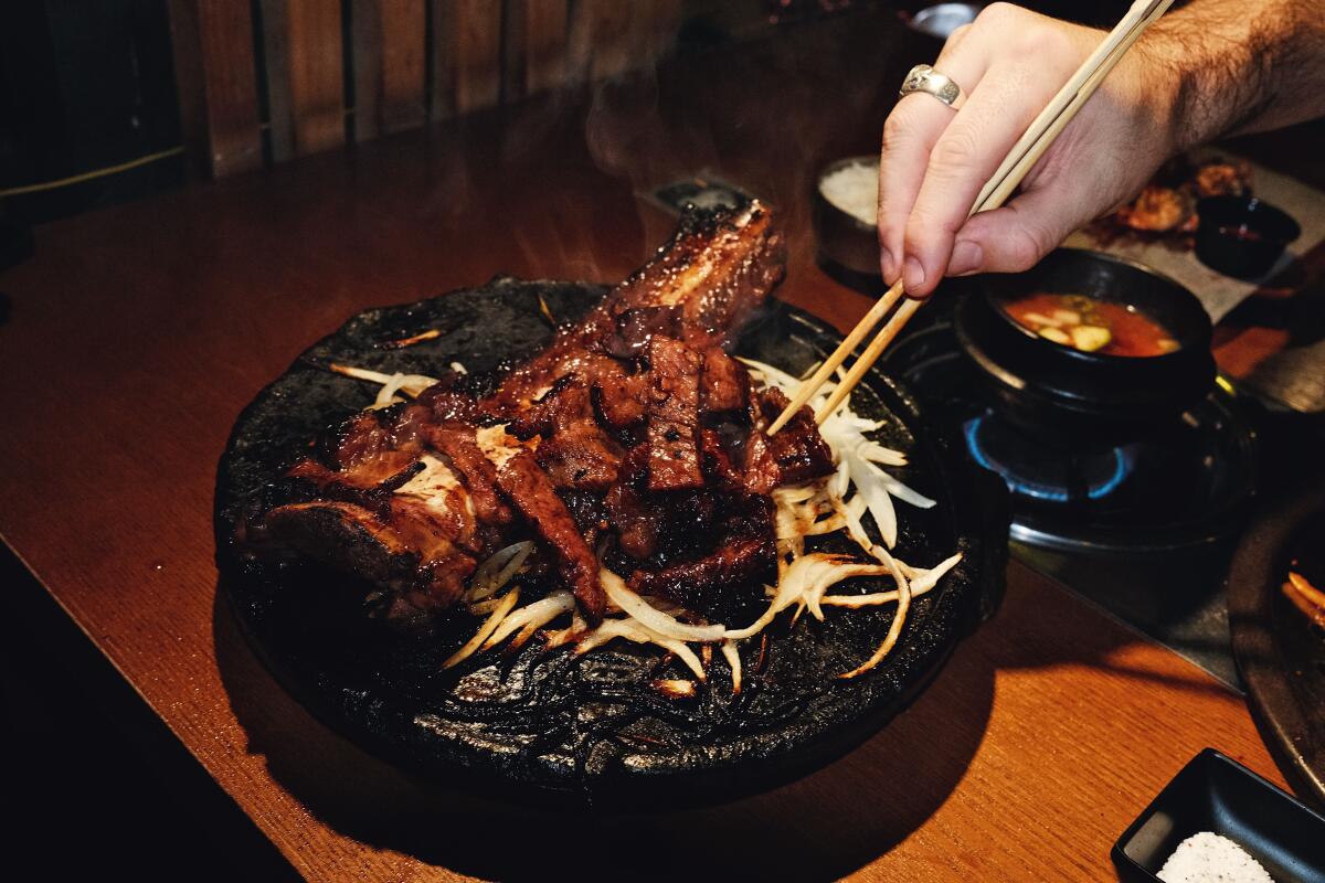 A hand with chopsticks reaches for the galbi tomahawk, massive bone included, on a sizzling tray at Woo Hyang Woo.