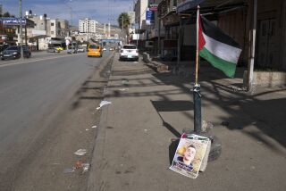Una bandera palestina y un cartel con la foto de Ammar Adili, de 22 años, quien fue baleado a muerte por un agente fronterizo israelí el viernes, en el lugar del incidente, en la principal vía en donde tiendas están cerradas en una huelga general en Hawara, Cisjordania, el sábado 3 de diciembre de 2022. (AP Foto/Nasser Nasser)