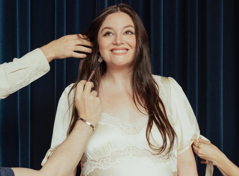 A woman in a dress gets primped for hair and makeup