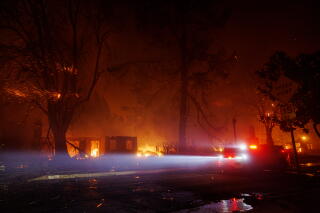 A police officer patrols the area as the winds continue to fuel the Eaton after midnight while multiple homes burn.