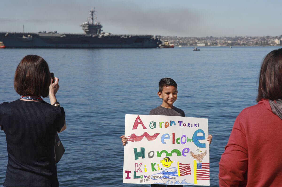 Aaron Roach holds a sign welcoming E-5 Kyle Roach back home during the arrival of the Carl Vinson 