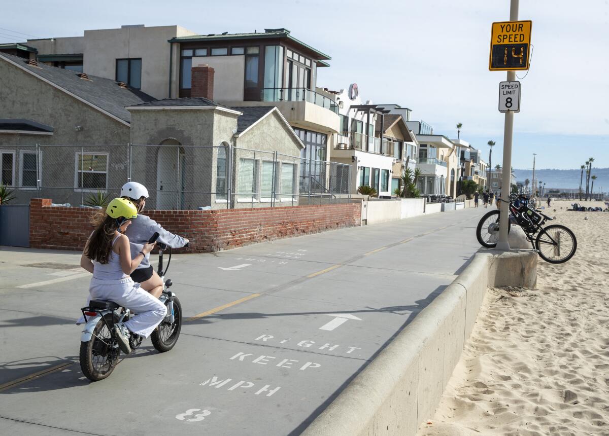 People ride an e-bike on the Strand in Hermosa Beach, where the posted speed limit is 8 mph.