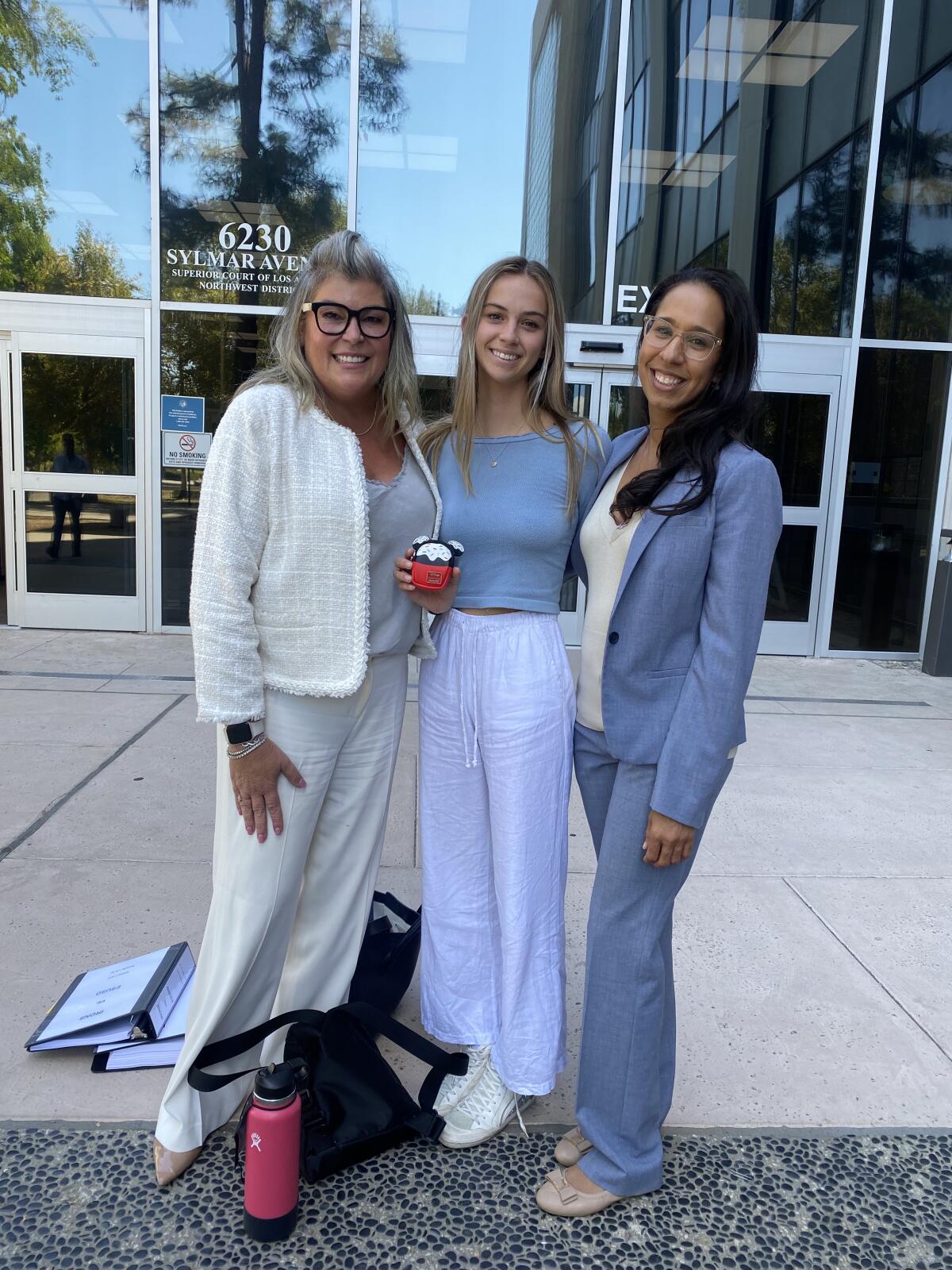 Two attorneys and a teenage girl smile in front of a courthouse