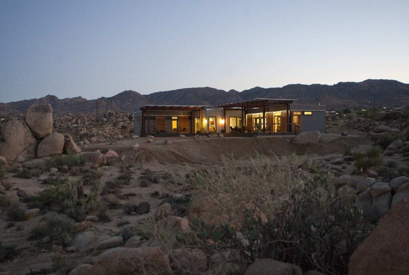 The low-slung prefab house built for Tim Disney by Blu Homes sits in the otherworldly landscape of Joshua Tree. The indoor-outdoor design, pictured here from the rear, includes generous shaded decks and a detached guest house, out of view here. Its prefab modules were built in less than eight weeks in a factory, then transported by truck and craned into place.