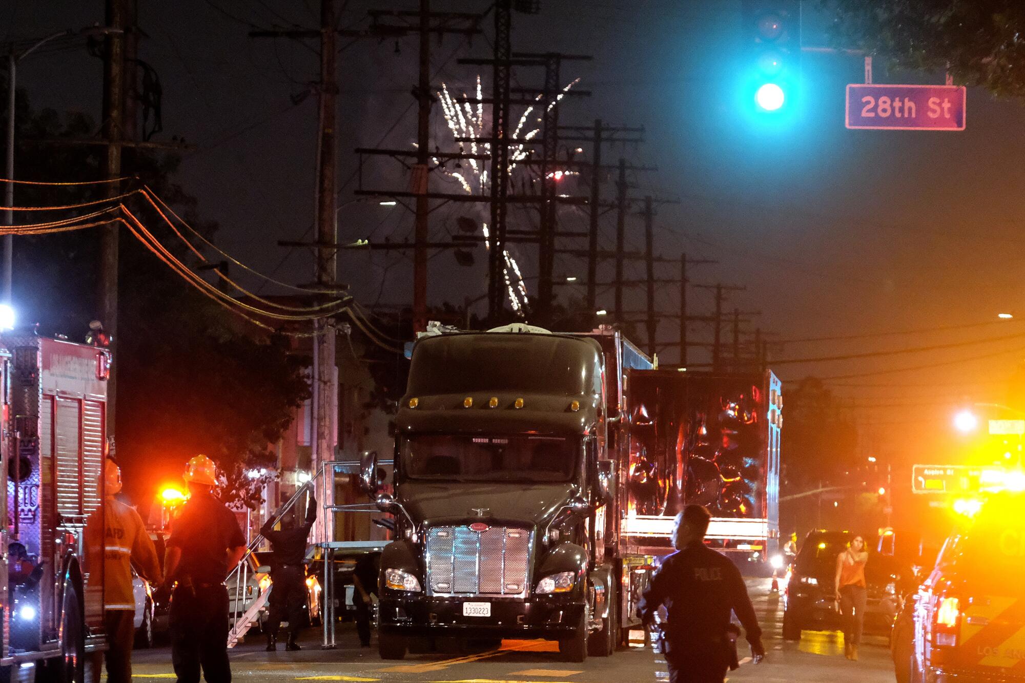 Fireworks in the sky as fire department and police vehicles surround a semitruck.