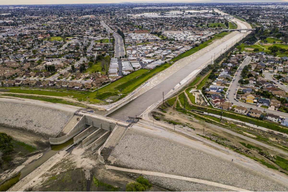 Aerial view of a dam at the end of a concrete flood channel running through a suburban landscape