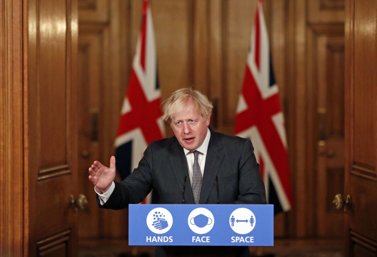 Britain's Prime Minister Boris Johnson speaks at a lectern adorned with images of hand washing, a mask and social distancing.