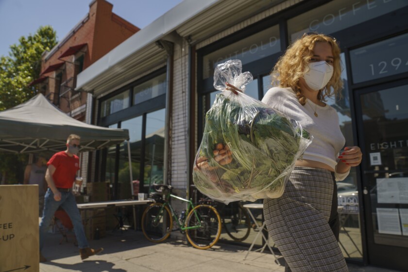Fashion designer Josie Vand wears a facemask as she retrieves a bag with organic vegetables from a farm box from County Line Harvest in Los Angeles on Friday, April 2, 2021. California has been easing COVID-19 restrictions as it recovers from a deadly winter surge, although public health officials still urge people to follow social distancing and mask-wearing protocols. Rates of hospitalizations and deaths have plunged, and the rate of people testing positive for the virus is at a near-record low. (AP Photo/Damian Dovarganes)