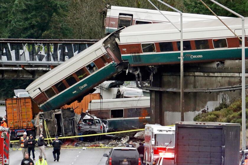 FILE - In this Dec. 18, 2017 file photo, cars from an Amtrak train lie spilled onto Interstate 5 below alongside smashed vehicles as some train cars remain on the tracks in DuPont, Wash. A conductor who was injured when a speeding Amtrak train flew off the tracks and onto a Washington state highway last month has filed a lawsuit Wednesday, Jan. 3, 2018, against the passenger rail company. Lawyers for Garrick Freeman of Bellevue, Wash., say Amtrak failed to provide a safe work environment. (AP Photo/Elaine Thompson, File)