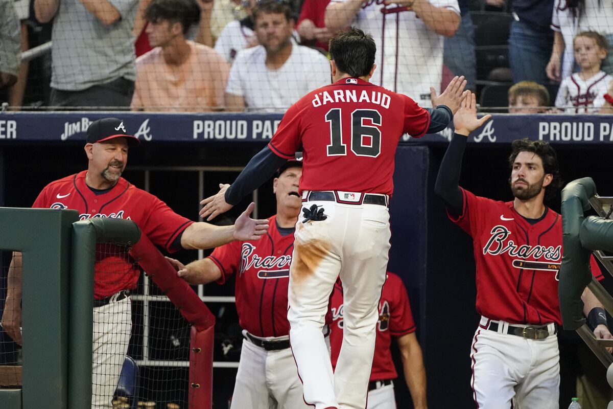 Atlanta Braves' Travis d'Arnaud (16) is greeted at the dugout by bench coach Walt Weiss, left, manager Brian Snitker, center, and Dansby Swanson, right, after scoring on an Ozzie Albies double during the fourth inning of a baseball game against the Pittsburgh Pirates on Friday, June 10, 2022, in Atlanta. (AP Photo/John Bazemore)