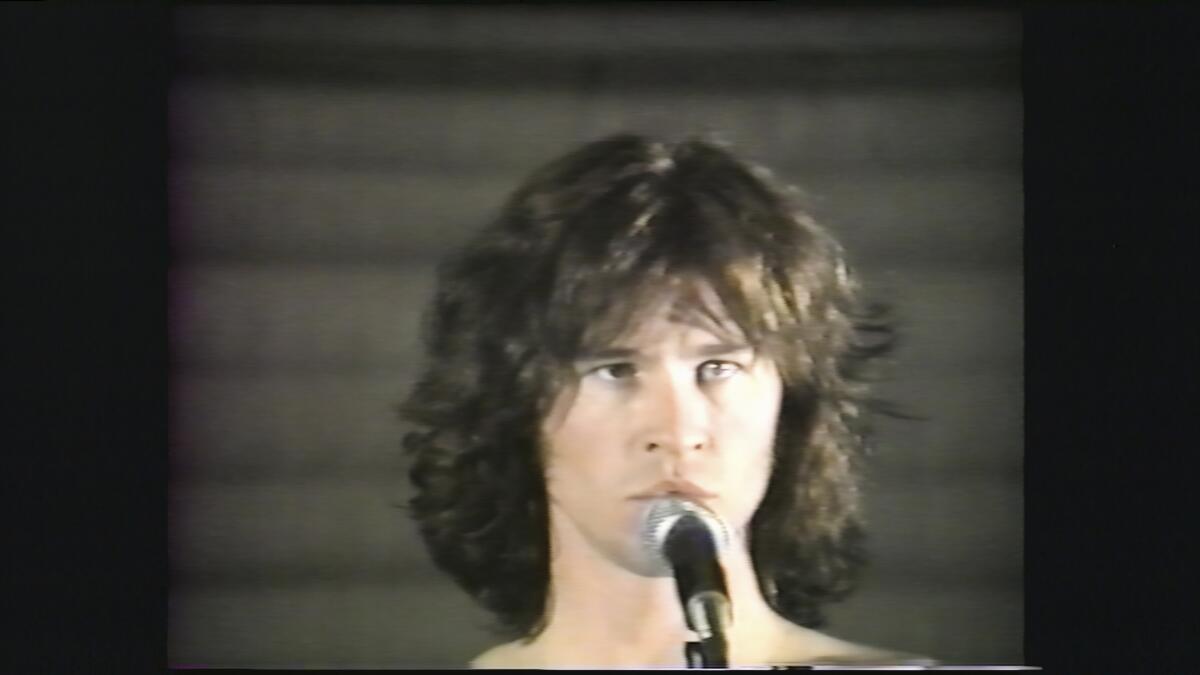 A young Val Kilmer stands in front of a microphone