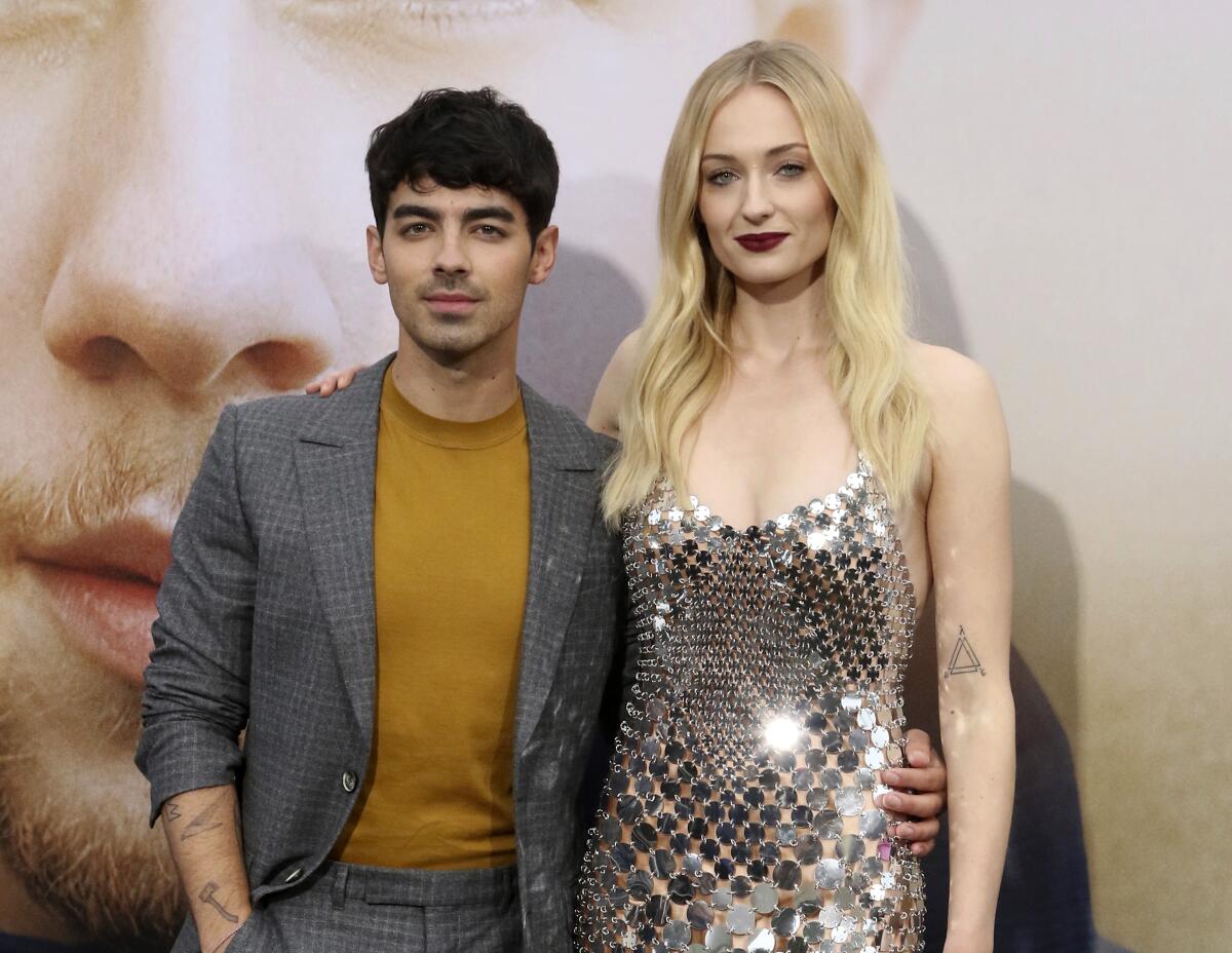 Joe Jonas, in a blazer, puts his arm around wife Sophie Turner, who wears a glittering silver dress