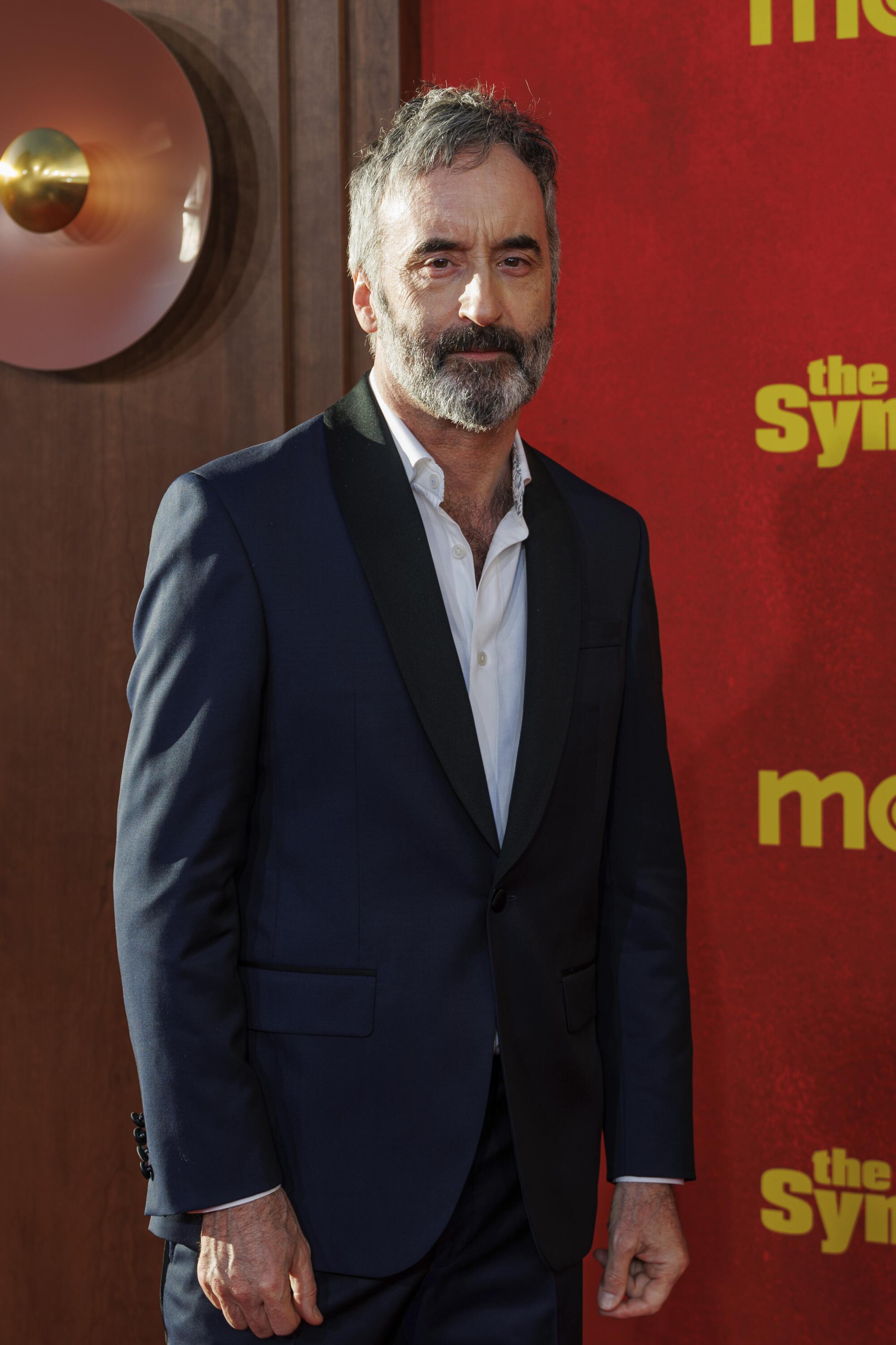 A man in a suit stands in front of "The Sympathizer" red backdrop.