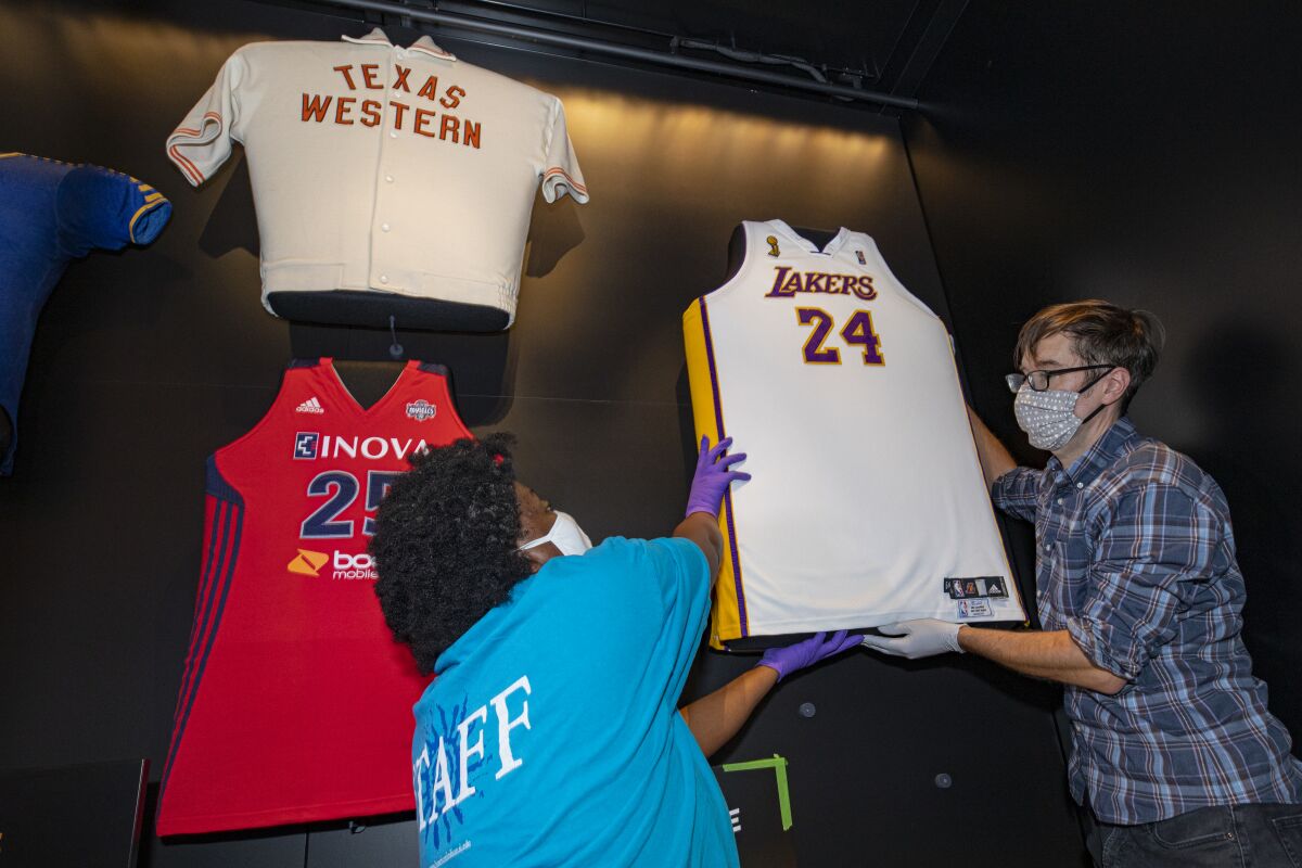 Two people hang up a Lakers jersey in a museum display