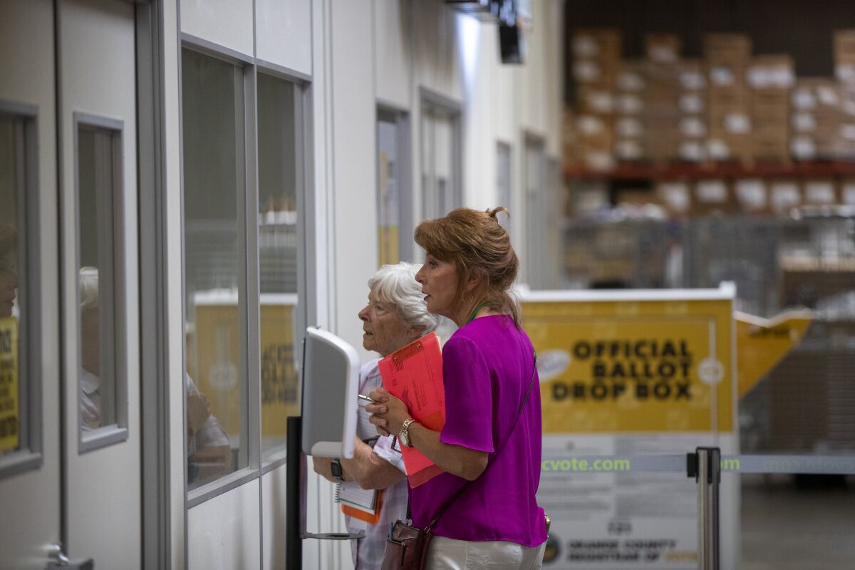 Two women election watchers look through a window where ballots are being processed.