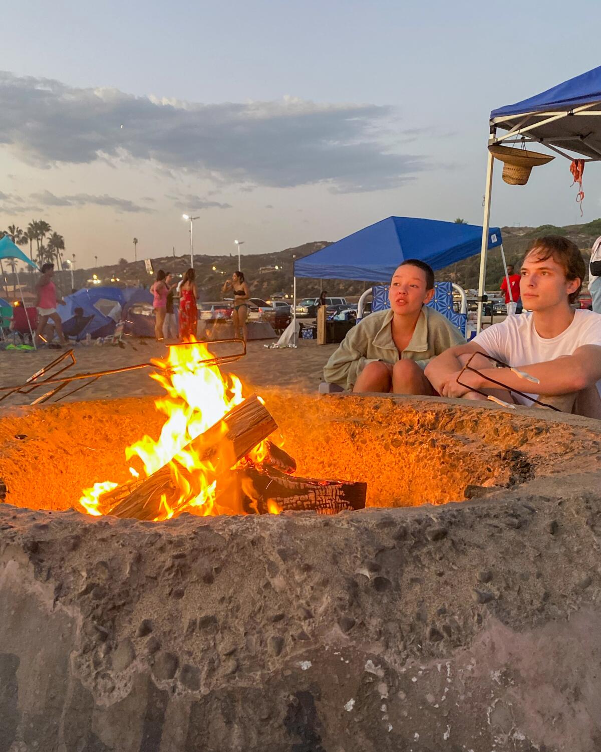People around a fire pit at a Southland beach.