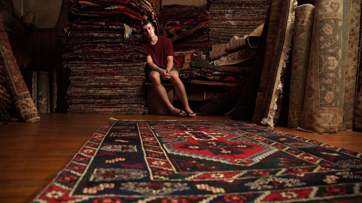 A man sits among persian rugs 