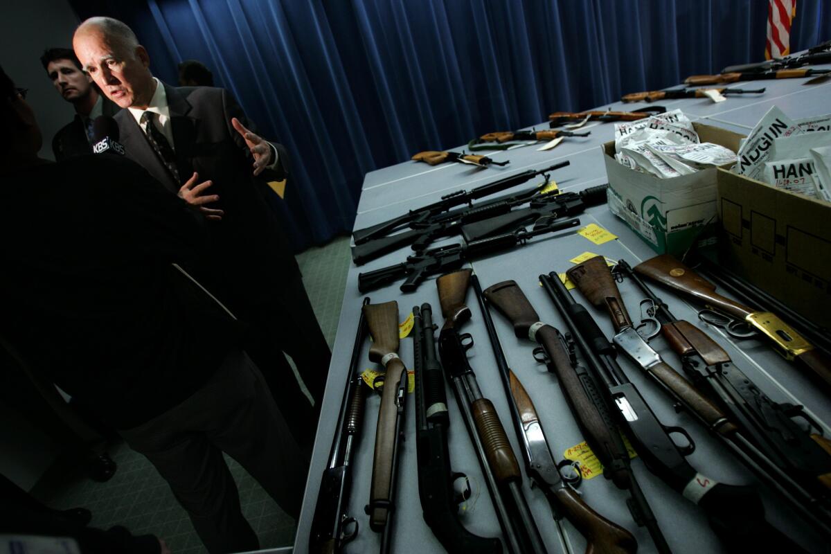 Spearking at Dec. 10, 2007, news conference in Los Angeles, Gov. Jerry Brown, then attorney general, shows guns seized from criminals during a law enforcement operation.