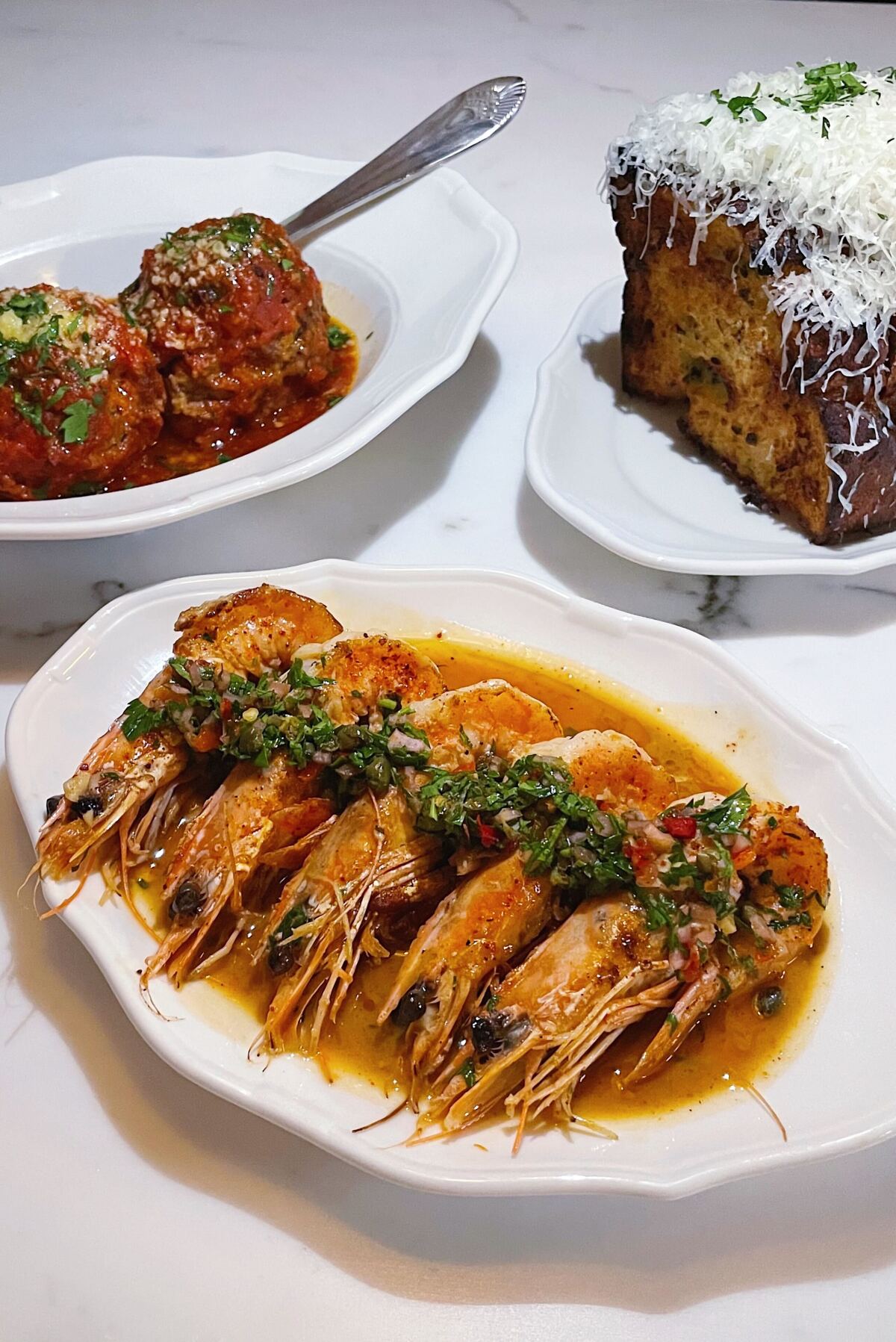 A vertical photo of head-on shrimp scampi, two meatballs, and parm-topped garlic bread from Donna's restaurant in Echo Park