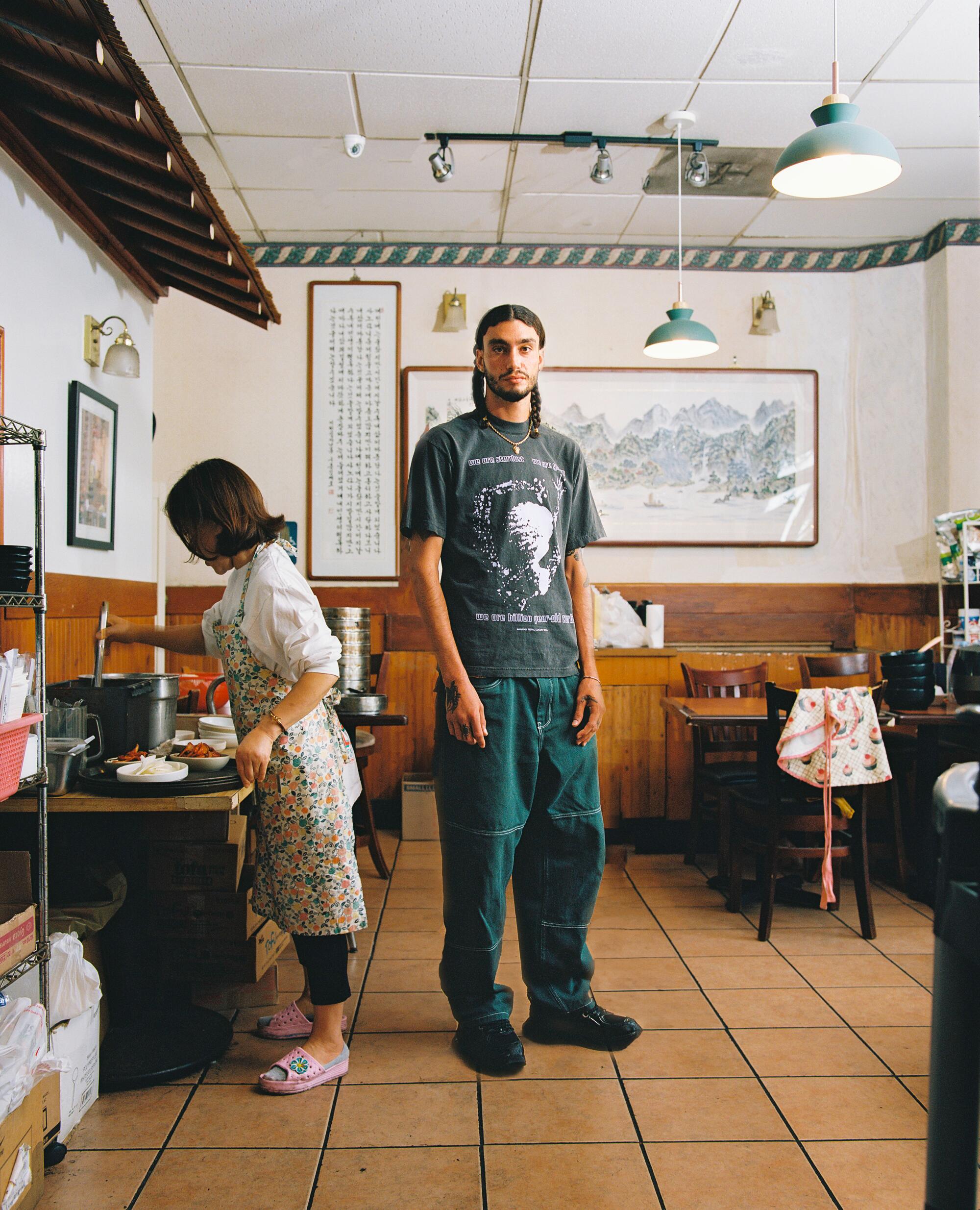 A man in a T-shirt and jeans stands in the middle of a restaurant.