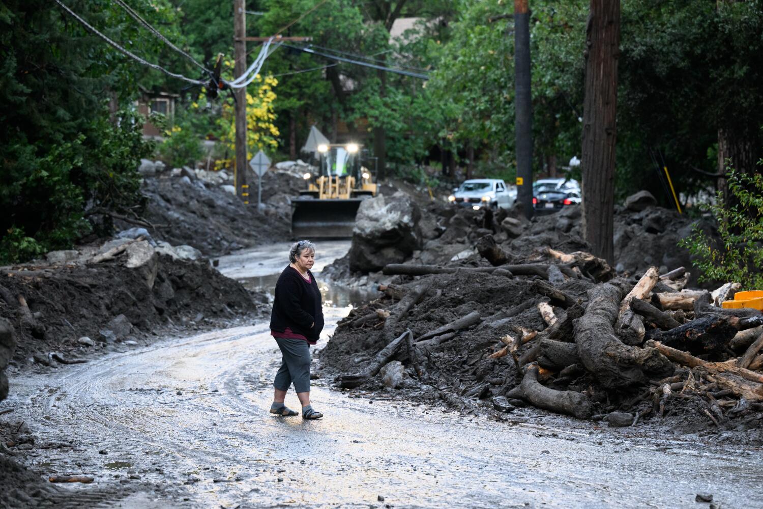 FOREST FALLS, CALIFORNIA - SEPTEMBER 19, 2025: A woman watches as workers clean debris from mudslides that were triggered by a tropical storm Friday, Sept. 19, 2025, in Forest Falls, Calif. (William Liang / For the Times)
