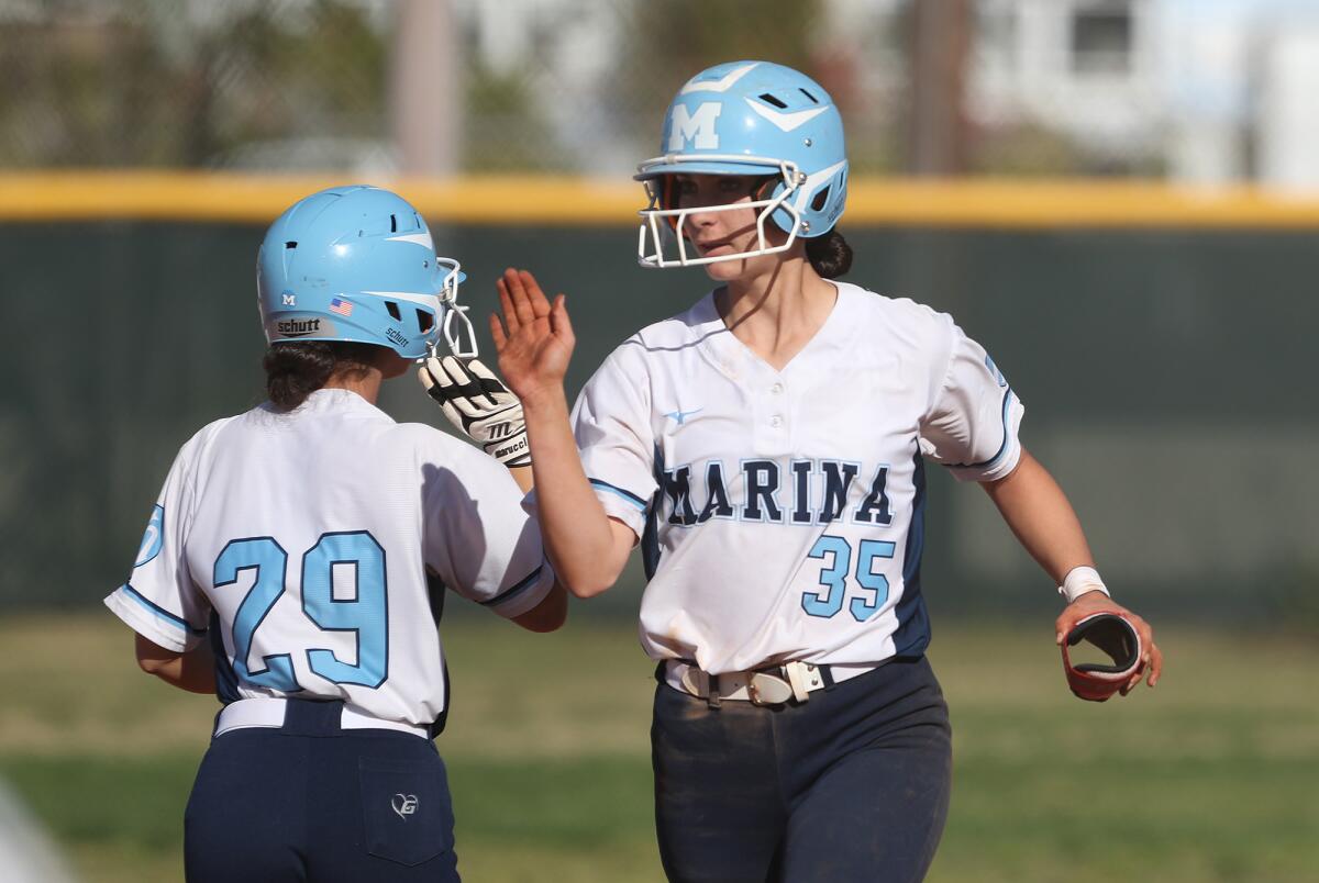 Marina's Zoe King (35) high-fives courtesy runner Preslee Brower during a Surf League softball opener against Edison.