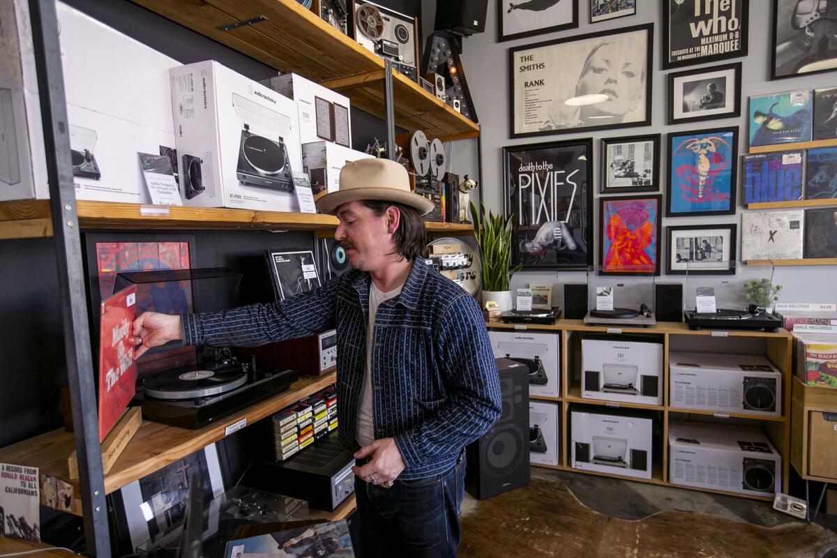 Josh Hertel, an employee at Analog Record Shop, puts a vinyl record on a player.