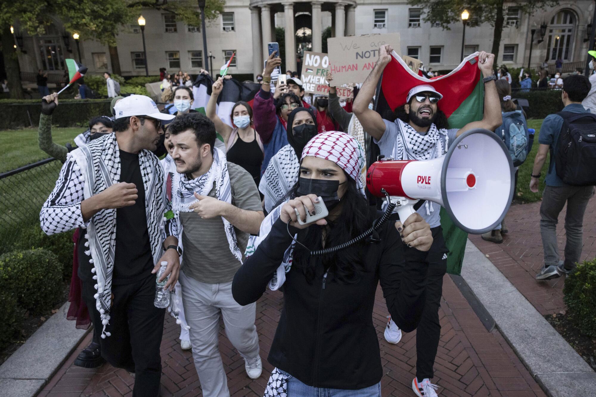 A person with a megaphone walks with a group of demonstrators on a college campus