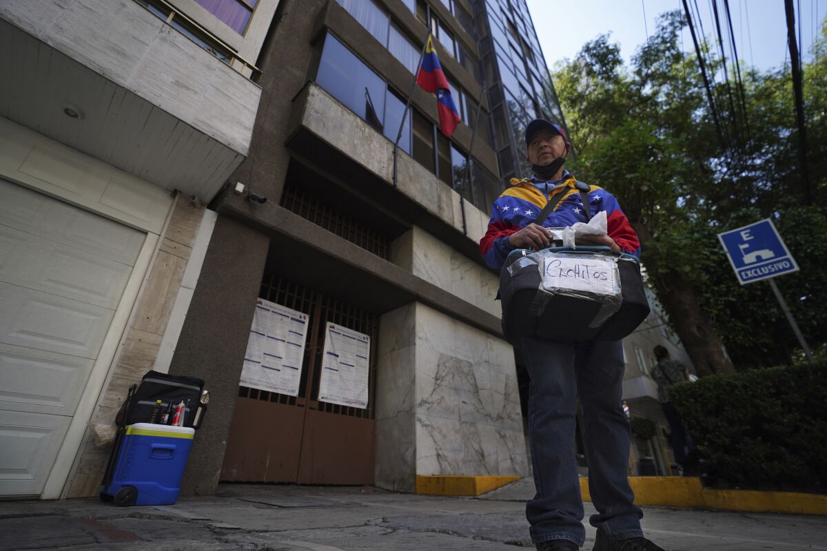 Venezuelan migrant Nelson Banda sells empanadas and cachitos in front of the Venezuelan embassy in Mexico City, Wednesday, April 20, 2022. Banda says he sells about 80 empanadas, a savory, crescent-like bread stuffed with ham, and and 40 of the other pastries a day outside the Venezuelan embassy as well as a non-alcoholic malt drink that is a staple at the Venezuelan breakfast table. (AP Photo/Marco Ugarte)