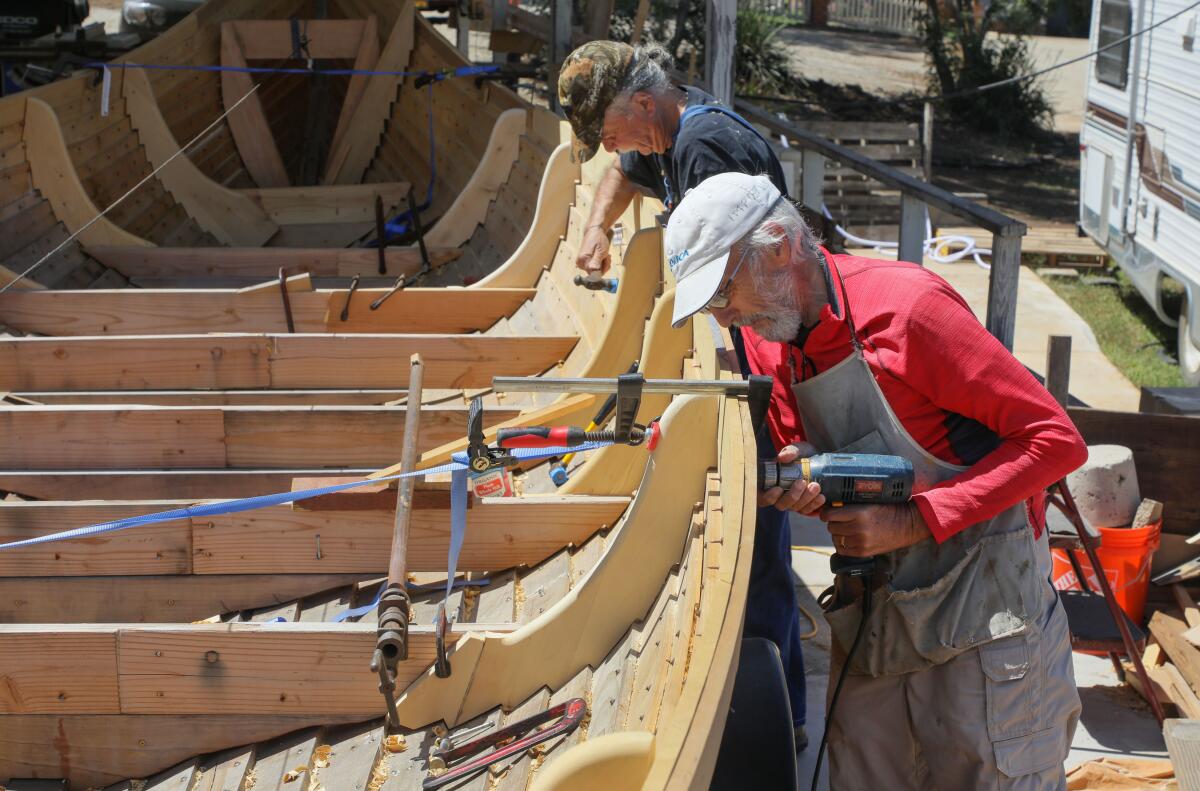 Two men install rivets in a Viking boat.