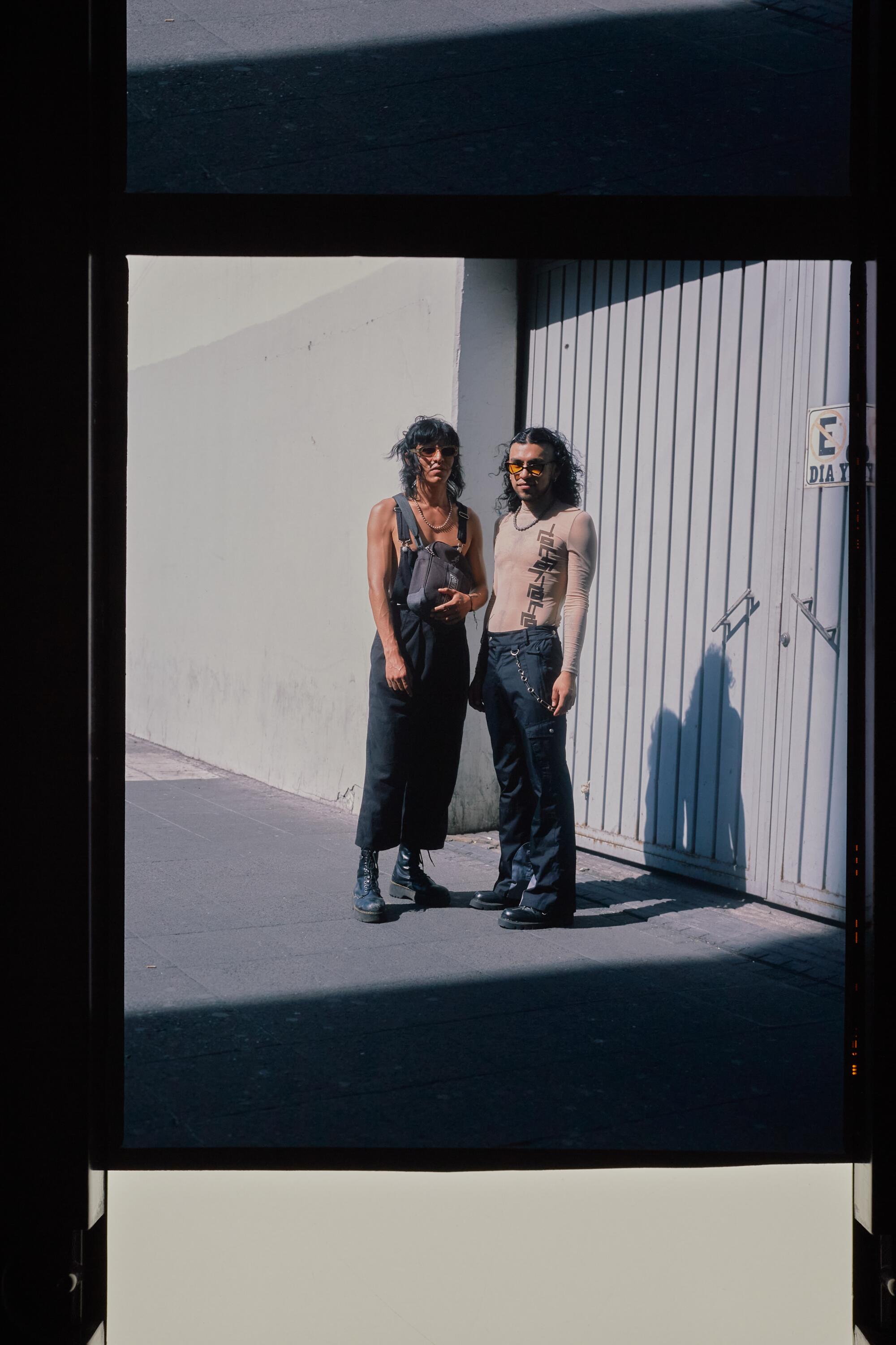 Two well-dressed people pose for a photo on the street.