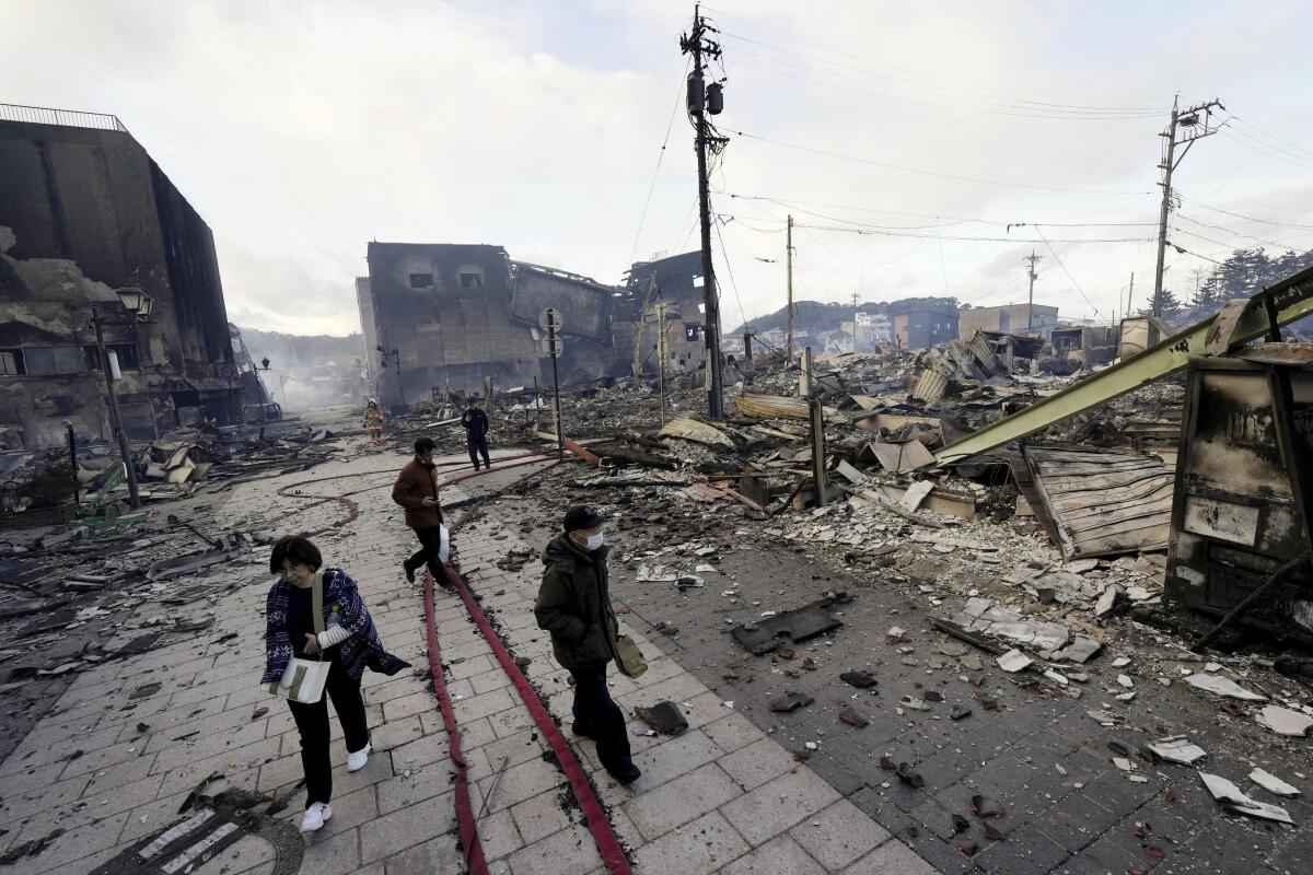 People walk past collapsed buildings in Wajima,  Japan.