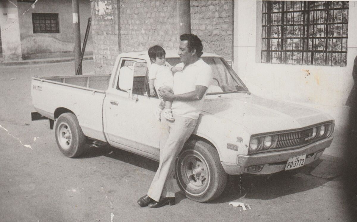 A man holds a child and leans against a pickup truck.