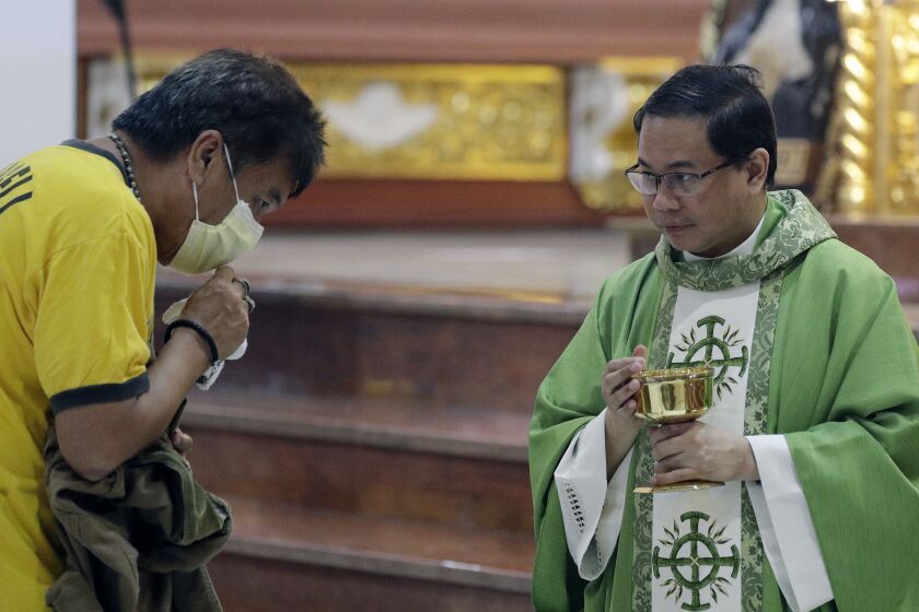 In this Feb. 10, 2020, photo, Catholic priest Fr. Joseph Arellano, right, looks at a man who forgot to take off his protective mask and tried to insert the host in his mouth during communion at a mass at the Minor Basilica of San Lorenzo Ruiz in Manila's Chinatown, Philippines. In a popular Catholic church in Manila, nearly half of the pews were empty for Sunday Mass. The few hundred worshippers who showed up, some in protective masks, have been asked to refrain from shaking or holding hands in prayers. (AP Photo/Aaron Favila)