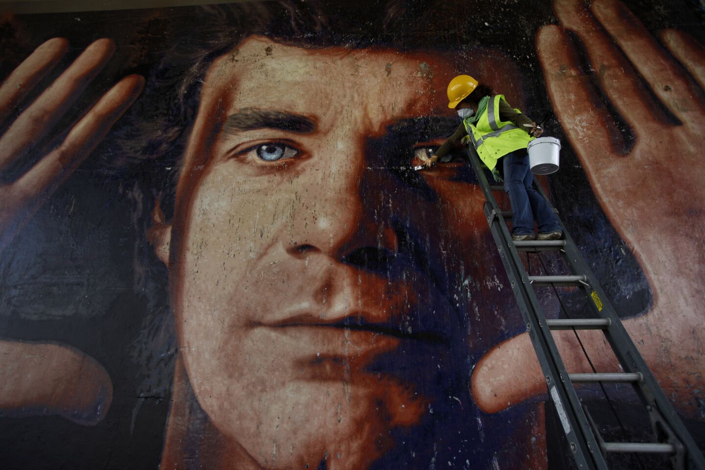 Virginia Panizzon, working with Save Freeway Murals in 2011, touches up Kent Twitchell's 1984 mural of art teacher Jim Morphesus. The mural, located along the Hollywood Freeway below the Grand Street overpass, had been defaced by graffiti.