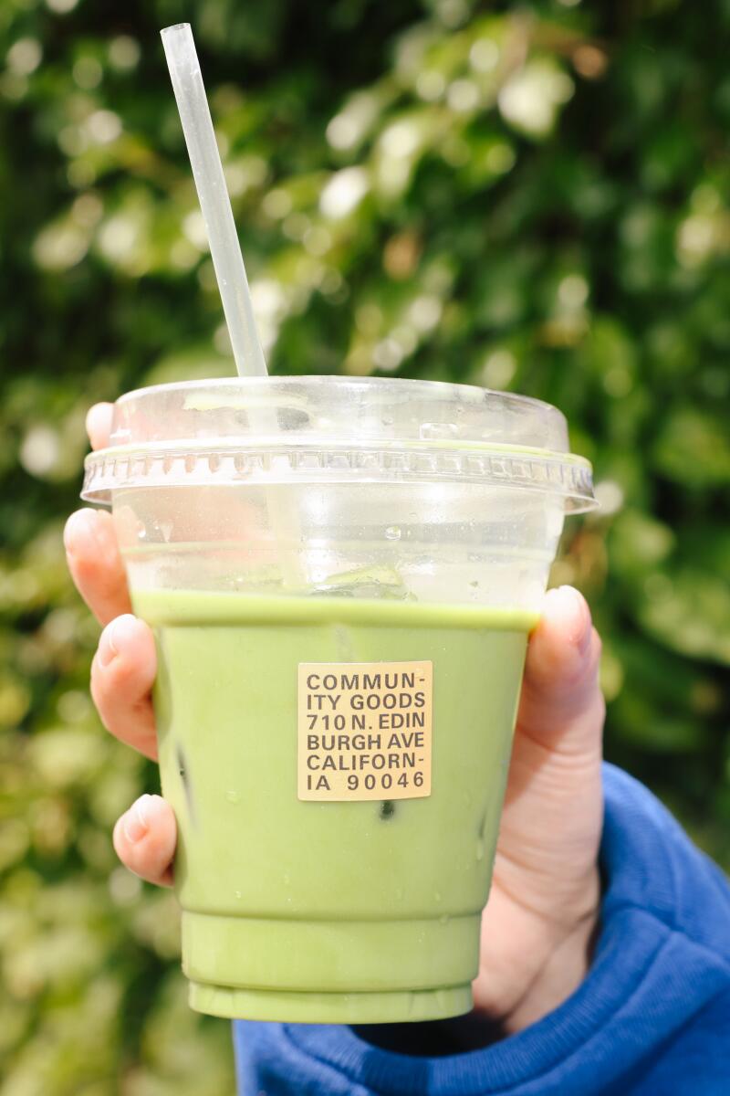 A hand holds up a green drink in a plastic cup.