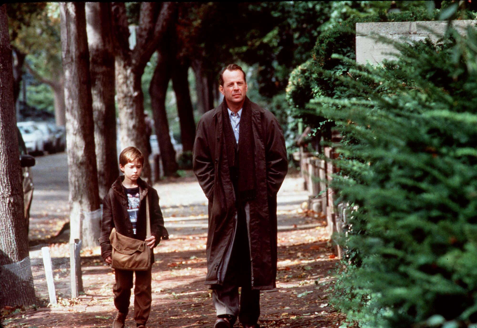 A boy and a man walk side by side down a tree-lined street.