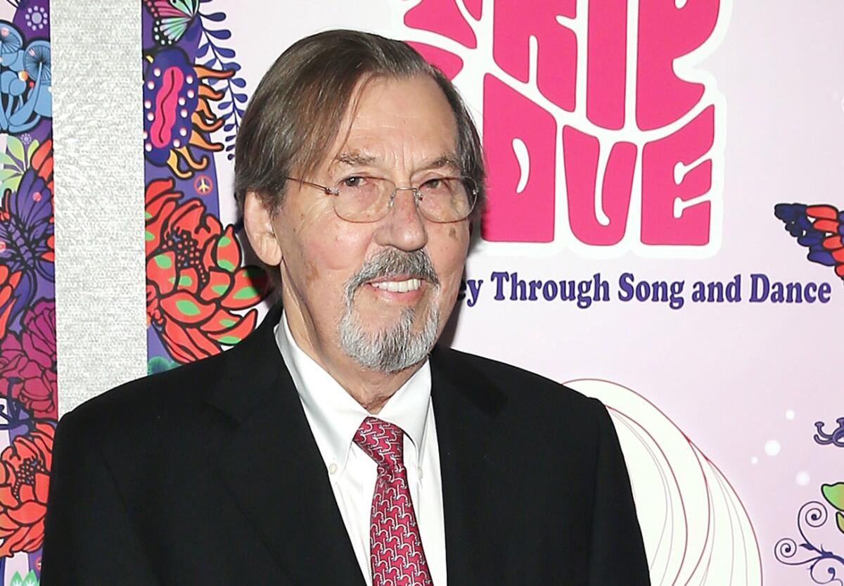 A man in suit and tie, with a goatee and glasses, in front of a colorful poster.