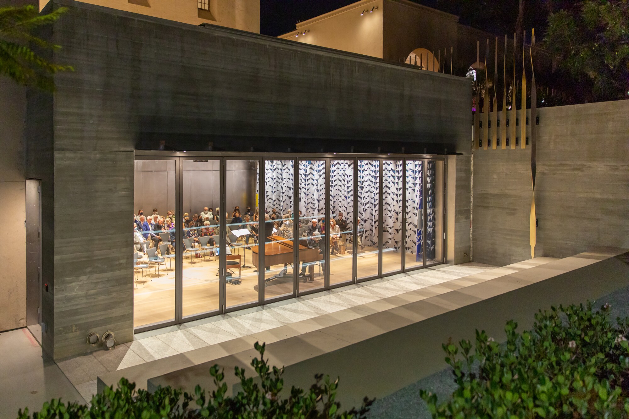 The Mingei's new theater space is seen at night from outdoors, illuminated from within.