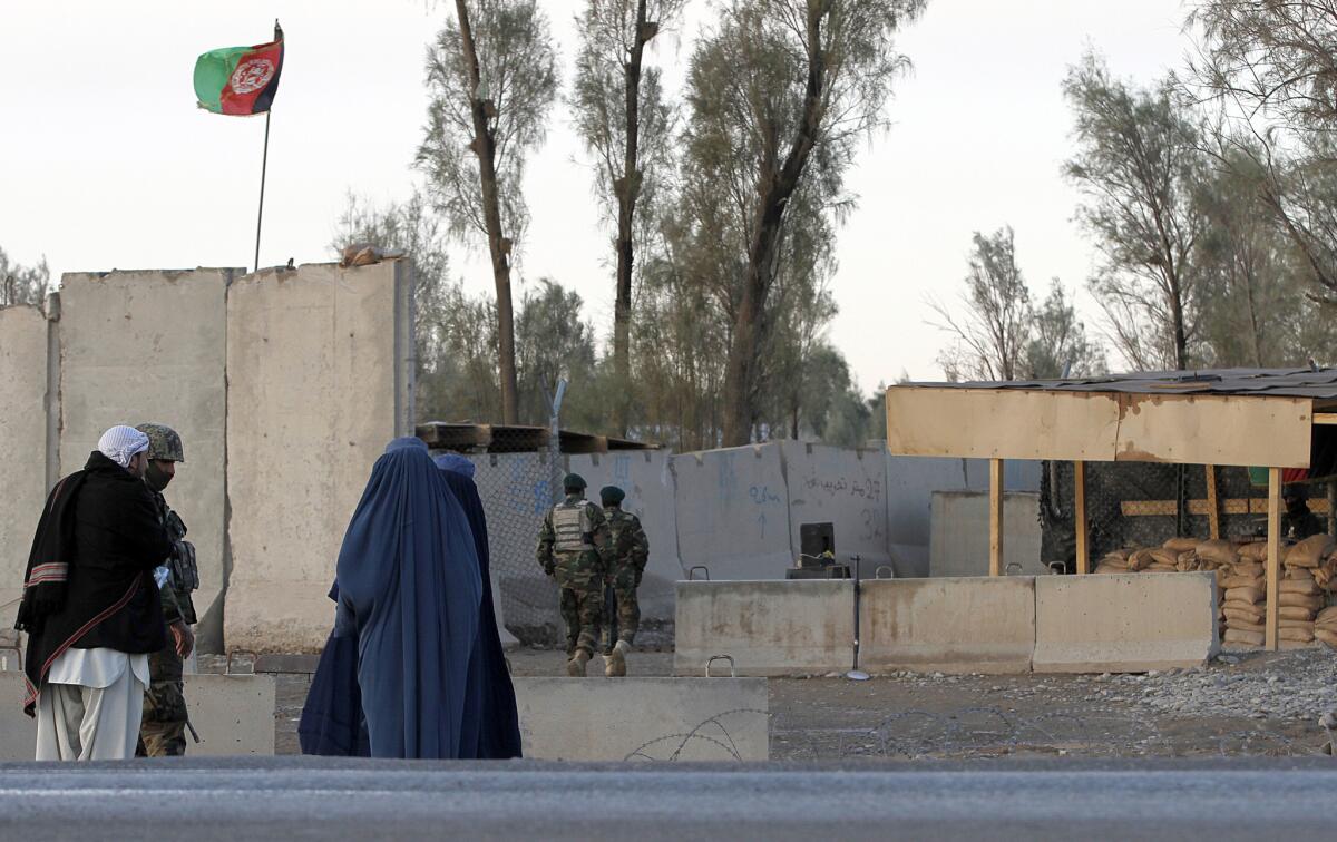 Civilians wait as Afghan security forces guard at the main gate of Kandahar airport during a clash between Taliban fighters and Afghan forces Dec. 9.